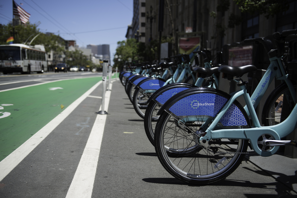 A set of turquoise blue bicycles sit in a special rack along on the curb of Market Street. A streetcar and American flag are in the background.
