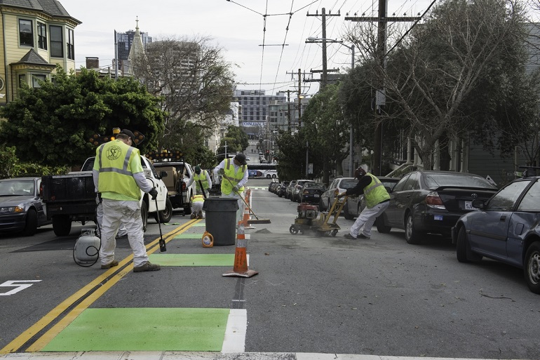 An SFMTA crew installs a bike lane in the center of Page Street with dashed green coloring and white striping.