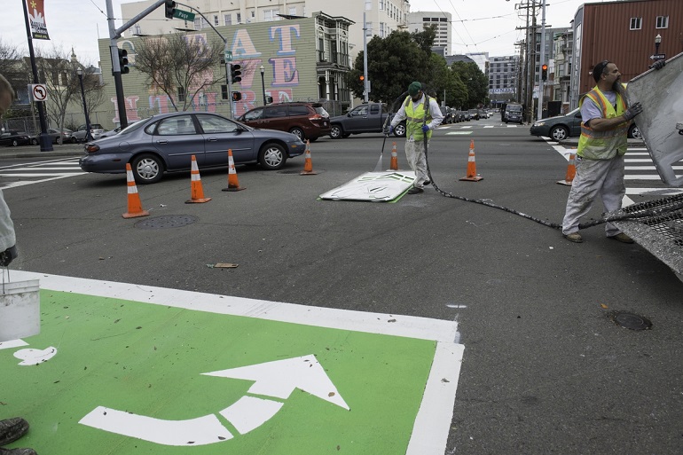 SFMTA crews install a green colored bike box with a left-turn arrow in the intersection of Page and Octavia.