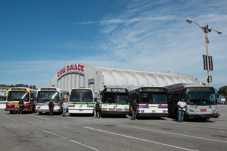 A row a modern and vintage Muni buses sit in front of the Cow Palace