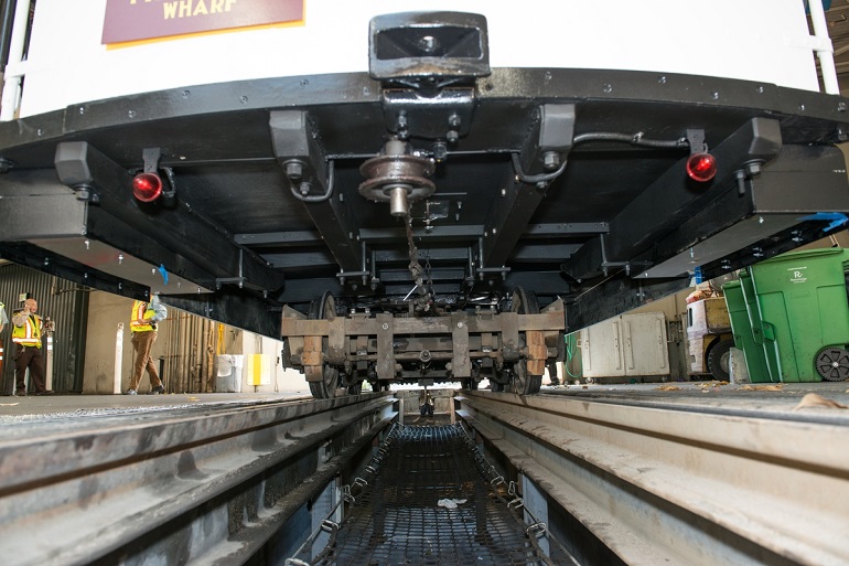 Photograph of the undercarriage of Cable Car 12 as it sits over a maintenance bay.