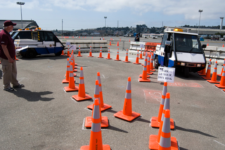 A photo shows a parking control officer driving a small, boxy, 3-wheeled vehicle through a narrow course of orange cones at the SFMTA Roadeo in 2008.