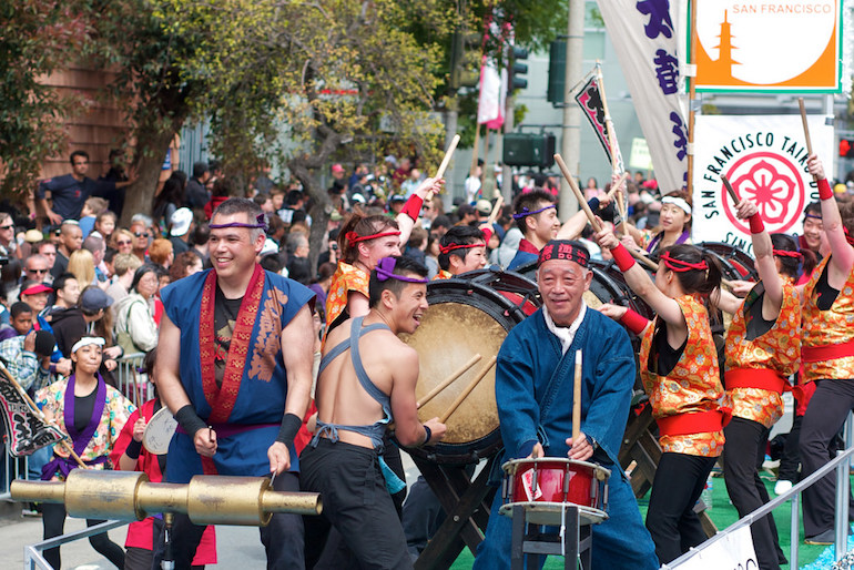 Men and women drum on traditional Japanese instruments while riding on a float in the Cherry Blossom Parade.