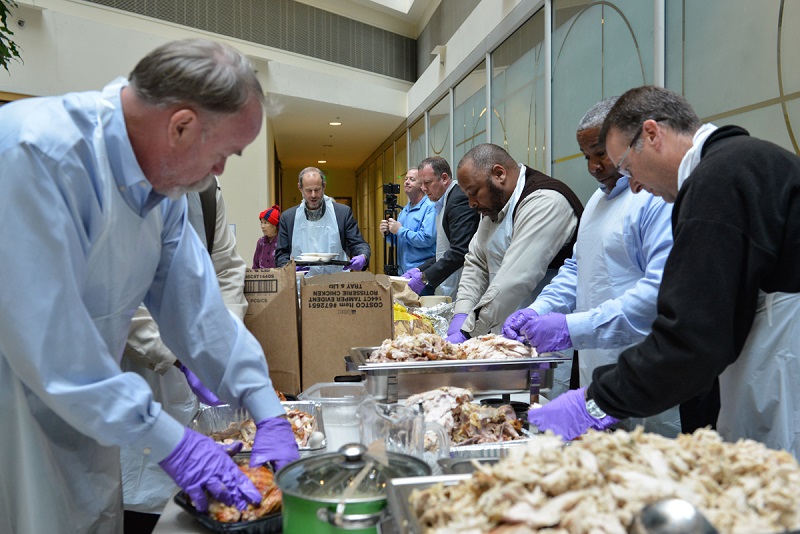 Several men stand around a long table preparing food.