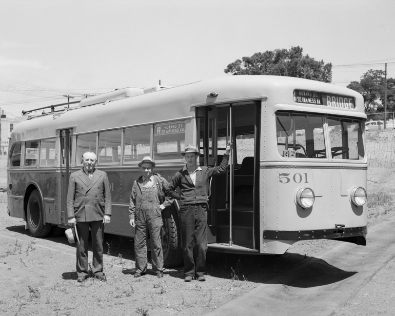 Black and white photo of three men standing in front of electric trolley bus in empty lot, taken on July 16, 1941.