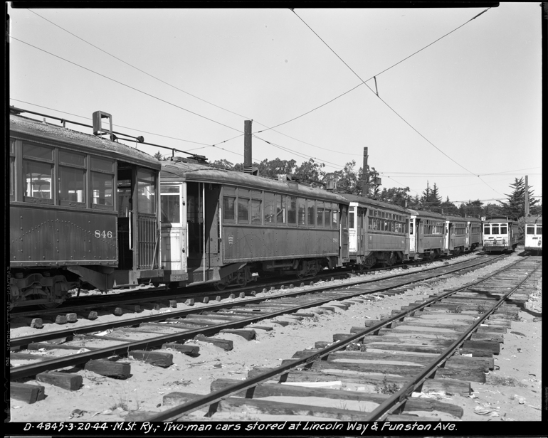 Black and white photograph showing row of old, worn streetcars sitting on tracks in an open lot.  Photo taken March 20, 1944.