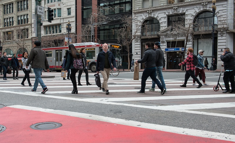 Pedestrians in a crosswalk along Market Street with historic downtown buildings a buses in the background.
