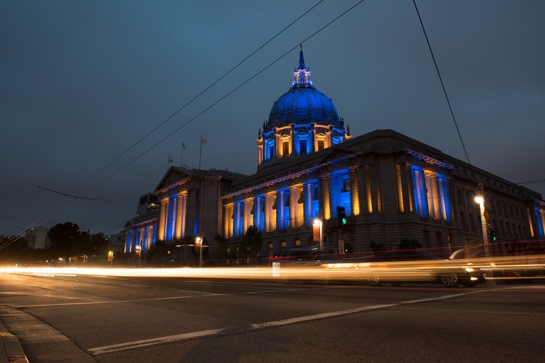 Low-angle photograph of City Hall at night lit in Warriors blue and gold.