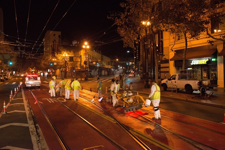 Paint crew in safety vests install red lanes on Market Street at night.