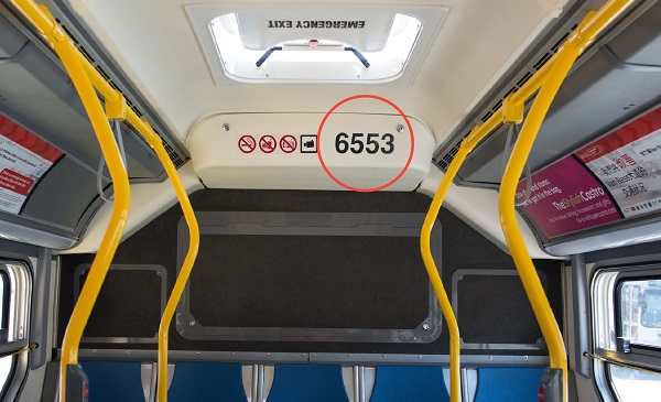 Interior of a new Muni bus with yellow stanchions. There is a red circle around the black four-digit number on the white back wall.