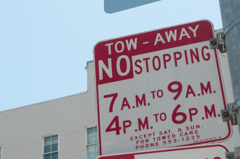 Low-angle photo of red and white "Tow Away, No Stopping" street sign with a blue sky in the background.