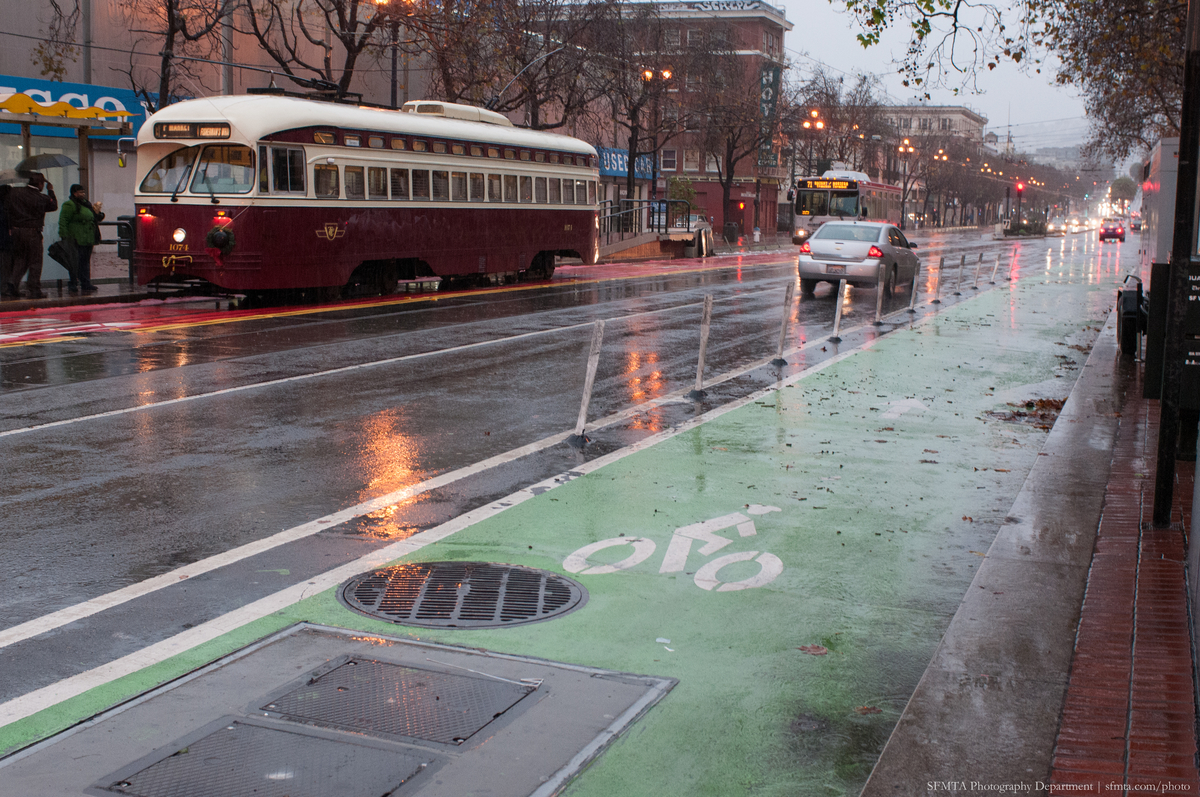 Market Street in the rain with a historic streetcar, car and green bike lane.