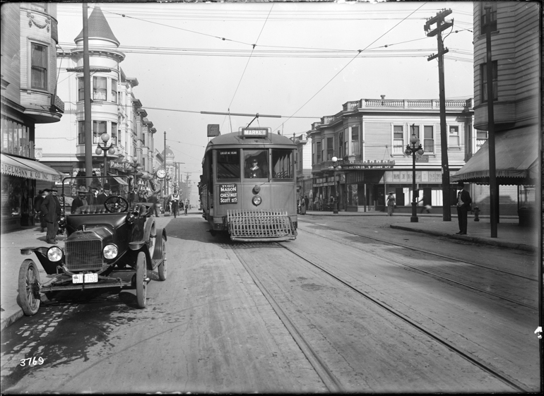 Black and white photo of a streetcar on the F Stockton line on Stockton Street, looking north from  just south of Vallejo Street, in late 1916. In the right foreground is a parked car, an early style Ford Model T. The street has pedestrians walking on both sides and street lamps with three large glass globes.