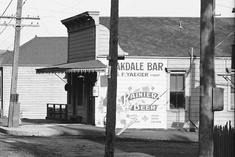 Detailed view from previous photograph showing flat-fronted building housing the "Oakdale Bar" the building is wooden with horizontal plank siding and a gabled roof.