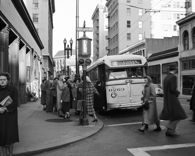 Black and white photo showing a group of people waiting to board a Muni bus in 1951.