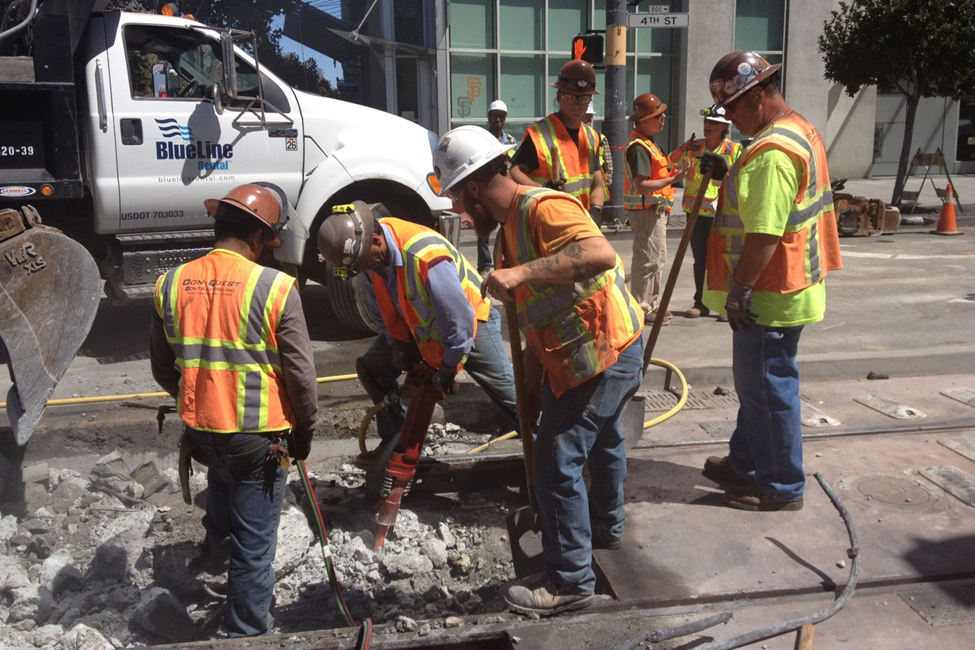 A construction crew in orange safety vests and hard hats demolishes pavement in the trackway on 4th Street.