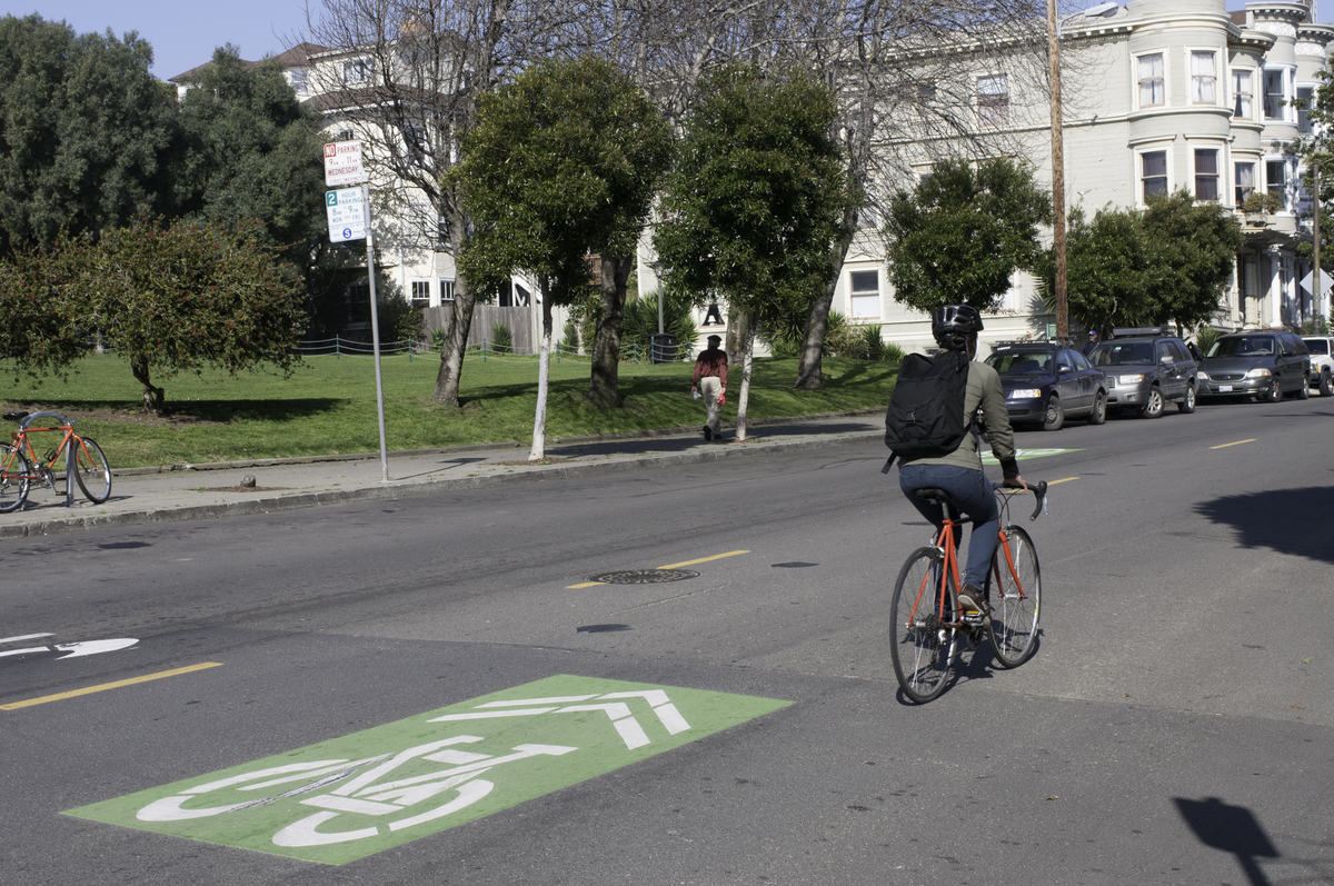 Bicyclist rides down a quiet street with trees and homes in the background.