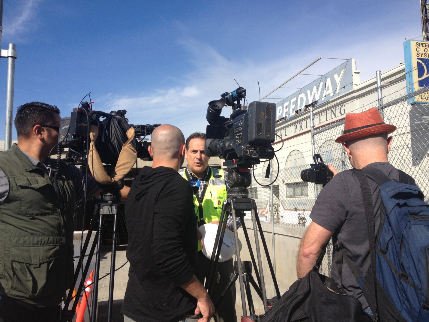 Man wearing a safety vest stands in front tv cameras and reporters.
