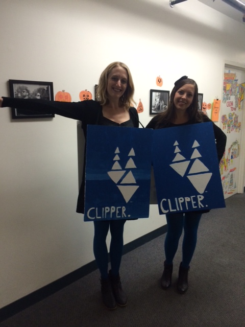 A blonde and brunette woman stand side by side with handmade blue sandwich board signs that read "Clipper"