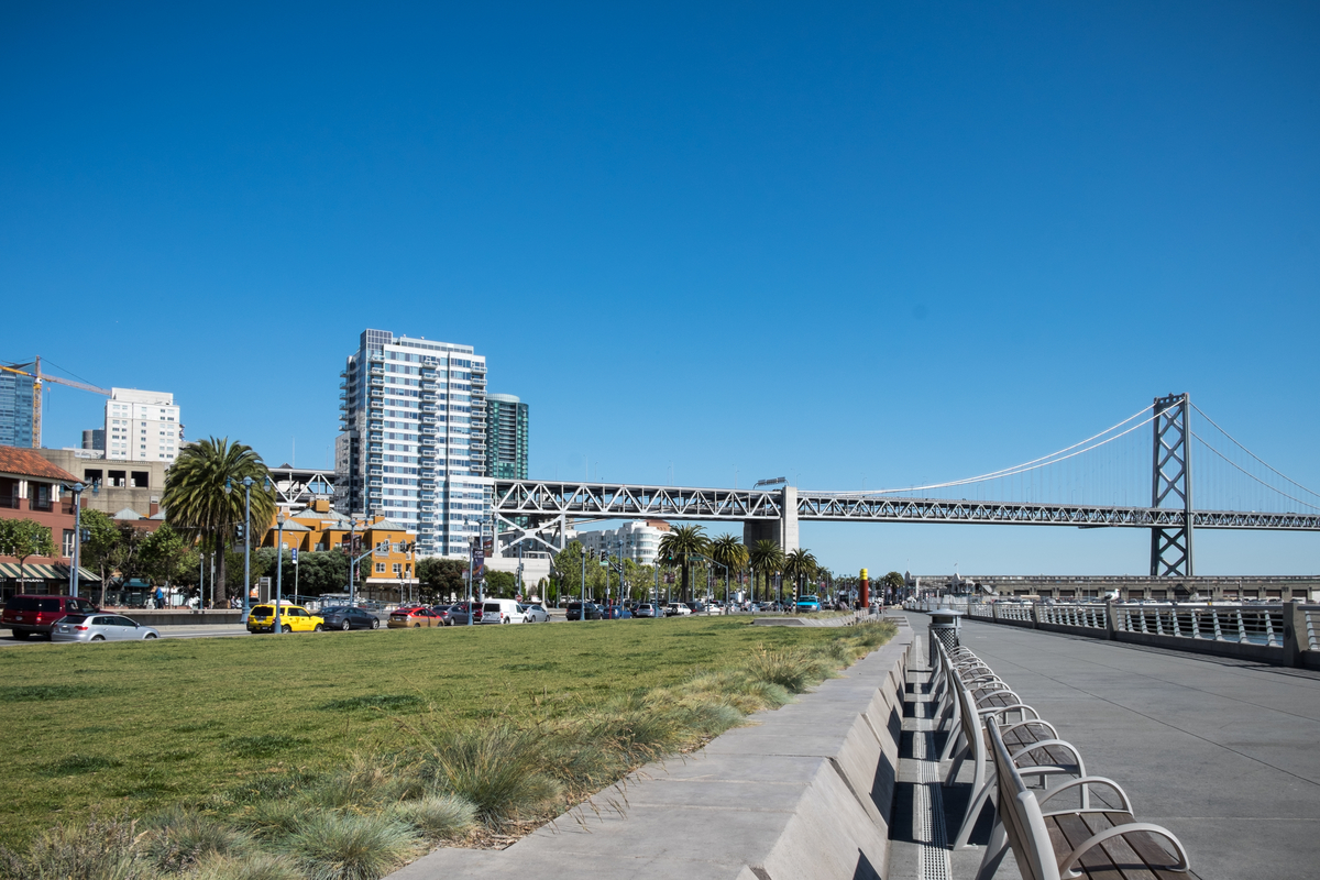 Bay Bridge and San Francisco waterfront along The Embarcadero with high-rises and cranes in the background.