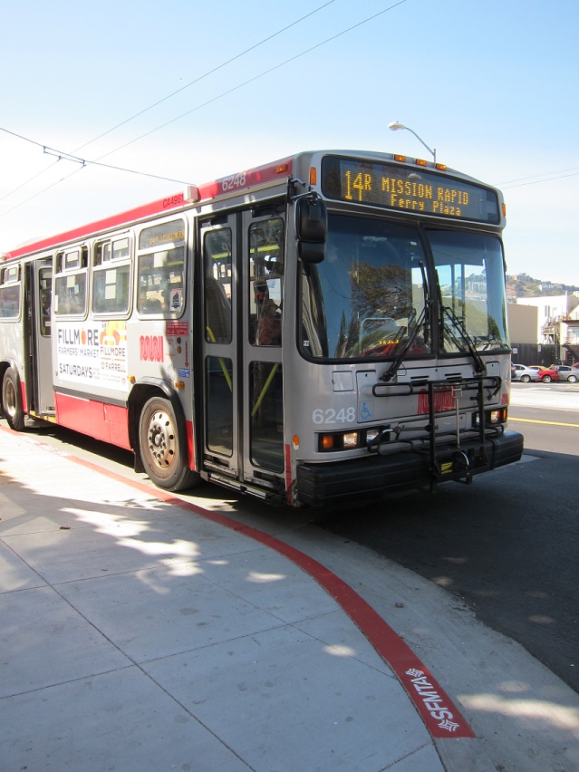 14R Mission Local red and gray Muni bus sits at a new pedestrian bulb on Mission Street.