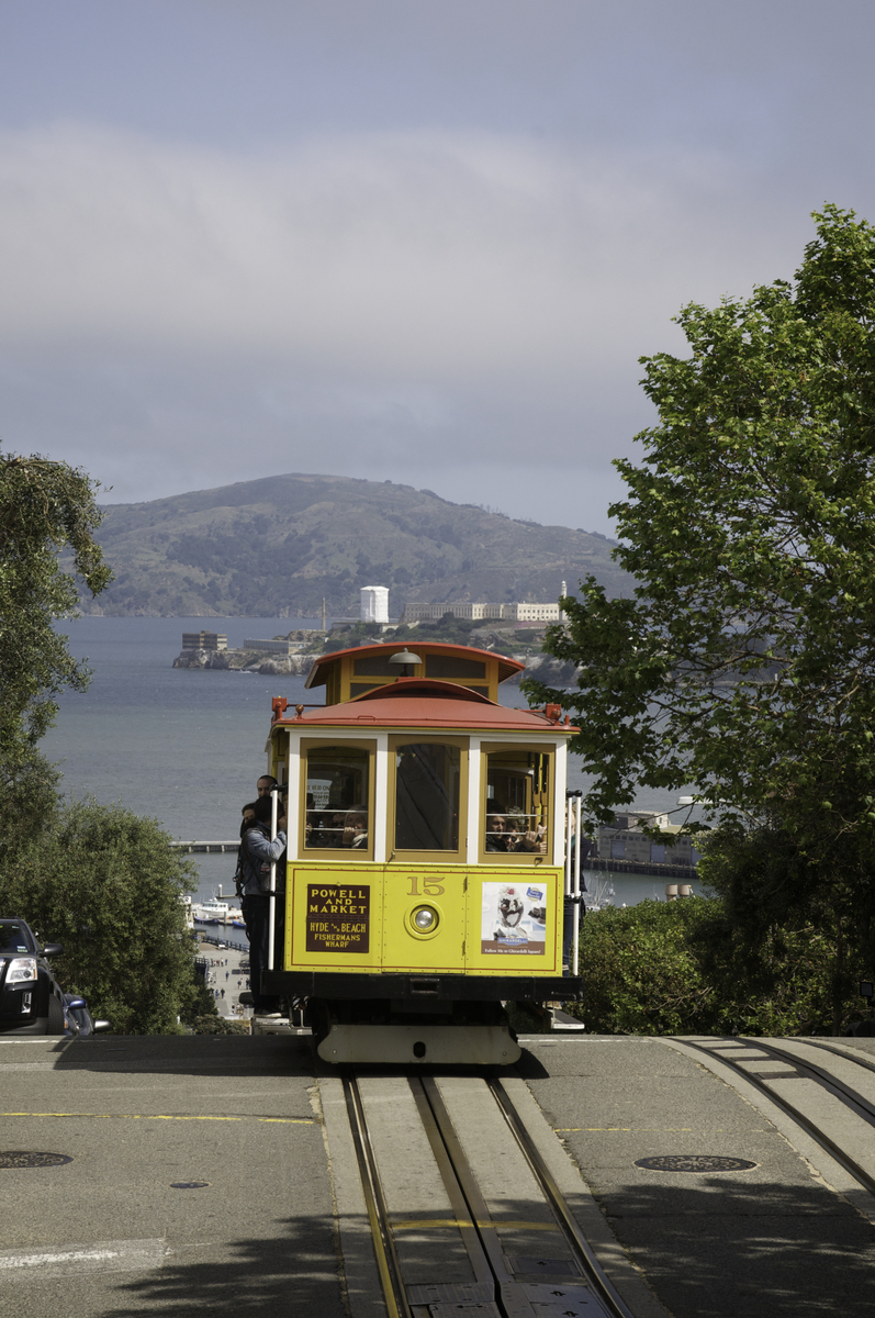 Yellow cable car 15 heads south on Hyde Street with Alcatraz and Angel islands in the background.