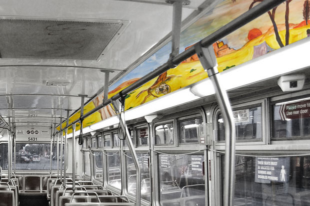 Black and white interior photo of a Muni bus with a color painting of a desert landscape along the top advertising space,