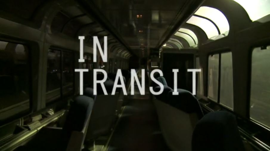 Dark interior shot of moving Amtrak train with large windows, white all caps text: "In Transit"