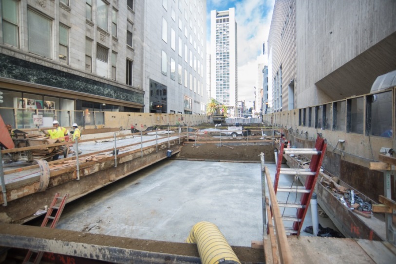 Construction site between downtown buildings wtih crew in safety vests and hard hats.