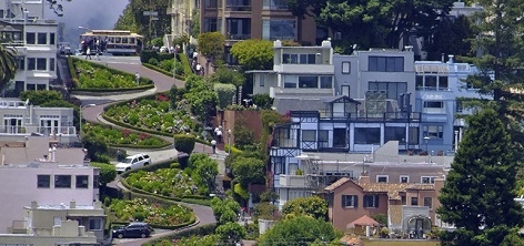 Lombard Street, the crooked street, from a distance surrounded by houses, with a cable car at the top of the hill.