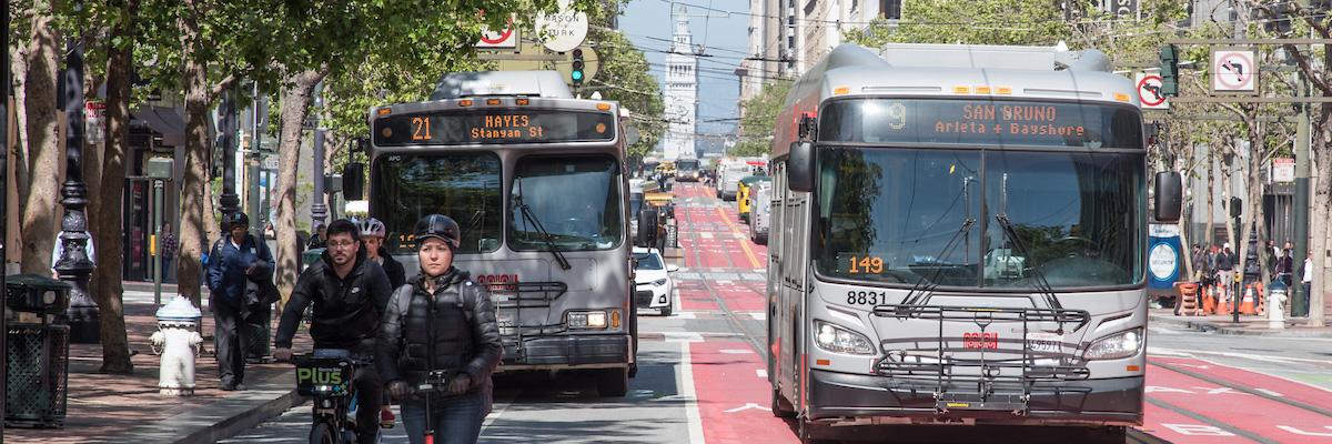 Market Street looking East to the Ferry Building Muni buses from 21 Hayes and 9 San Bruno behind people on a scooter and a bike
