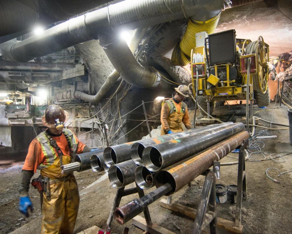 Two men ready a section of drill casing before lifting it up the ramp to the drill rig positioned as part of grouting work for t