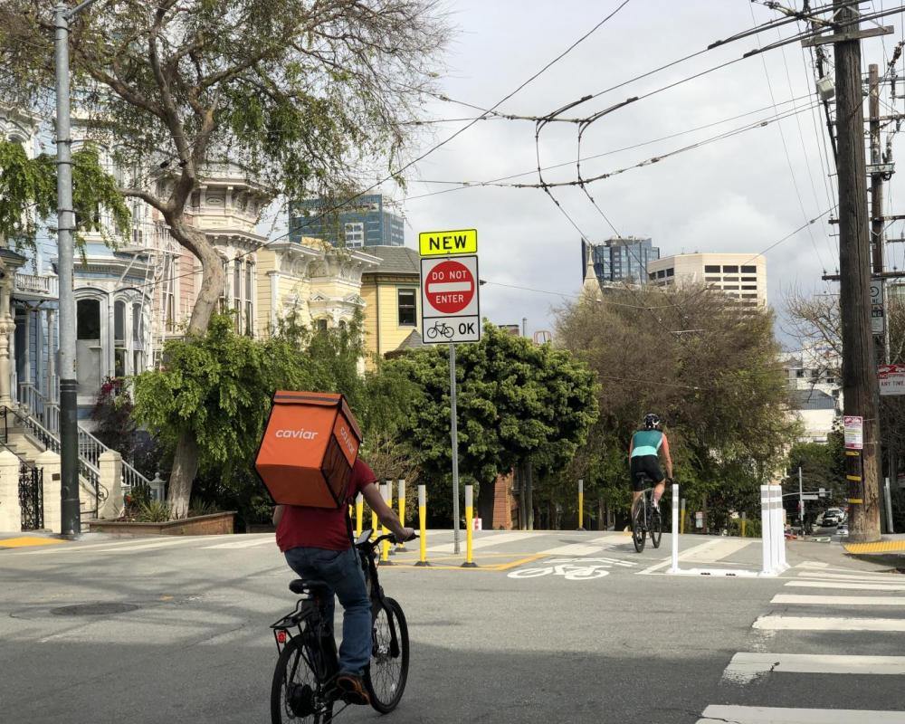 View of two people on bikes using the protected downhill bikeway on Page Street at Laguna Street, facing east toward Downtown