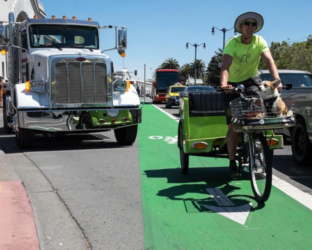 View of a pedicab driver riding in the northbound bike lane on The Embarcadero in front of Pier 35, looking south