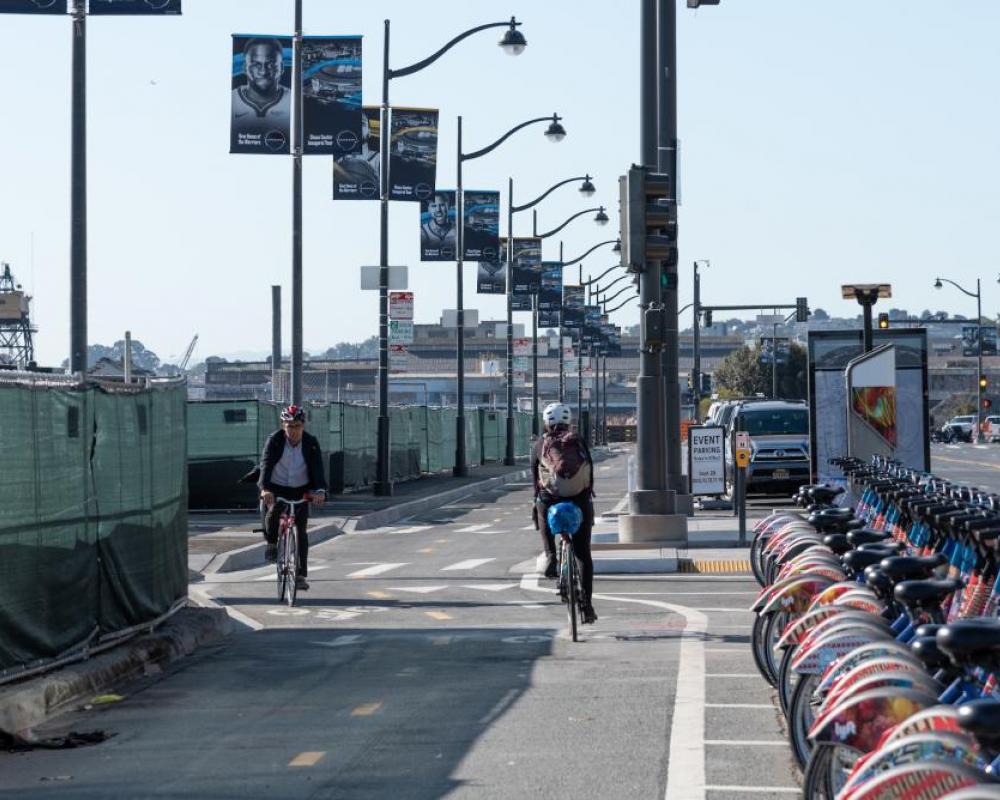 Two bicyclists in the two-way protected bikeway on Terry Francois Blvd. with a bikeshare station located in the buffer