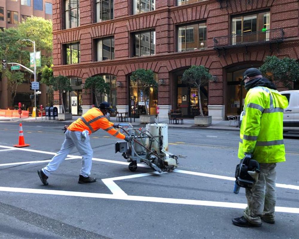 Two employees with equipment painting the road