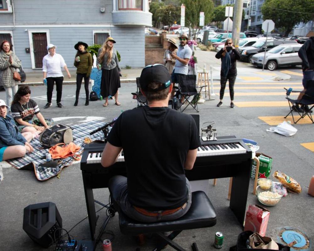 Community members on Page Slow Street stop and listen to a man playing piano in the street