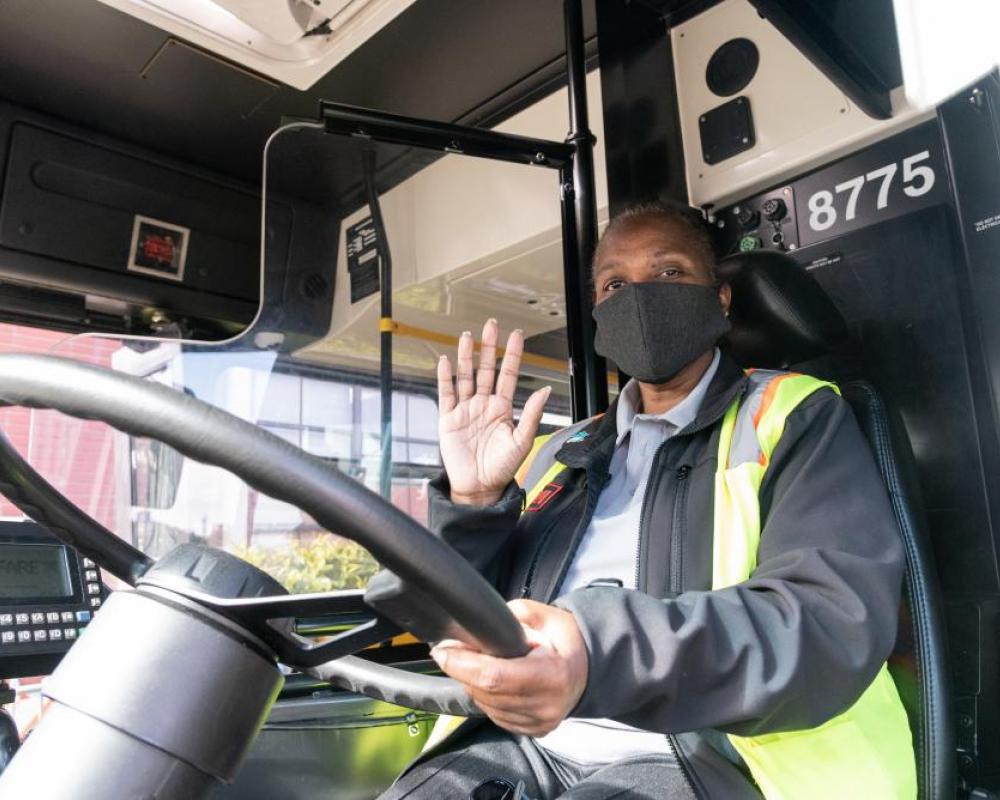 Operator waiving hello at the wheel of a bus