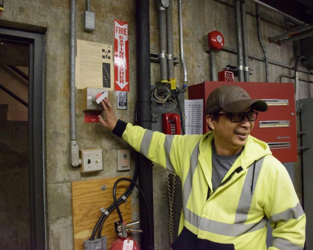 Crew member looking away while holding a wall switch inside a systems shop location.