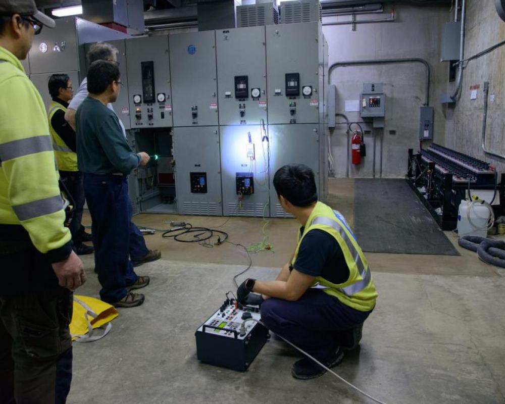 Several crew members inside a systems shop location looking at the cabinet wall. 