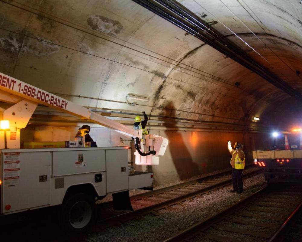 Work trucks along the tunnel wall with a crew member giving directions with their hands. 