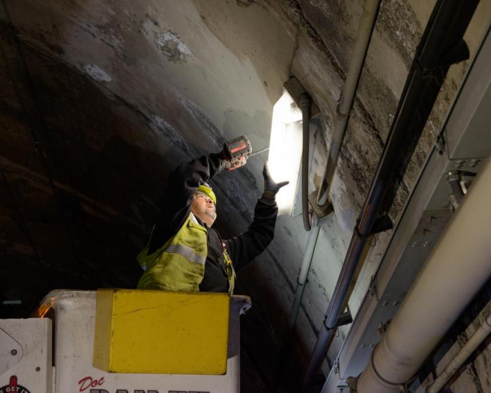 Crew member holding light by the tunnel ight. They seem to elevated by a lift. 