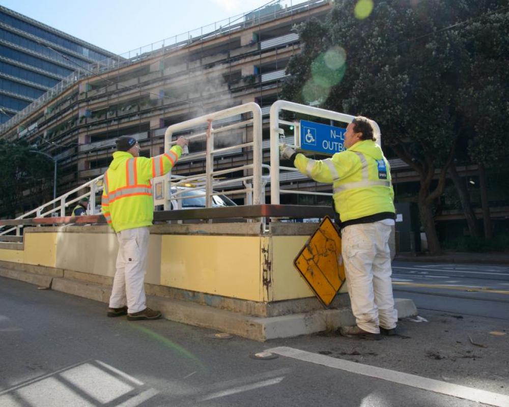 Two crew members by a wheelchair ramp with a building in the background.