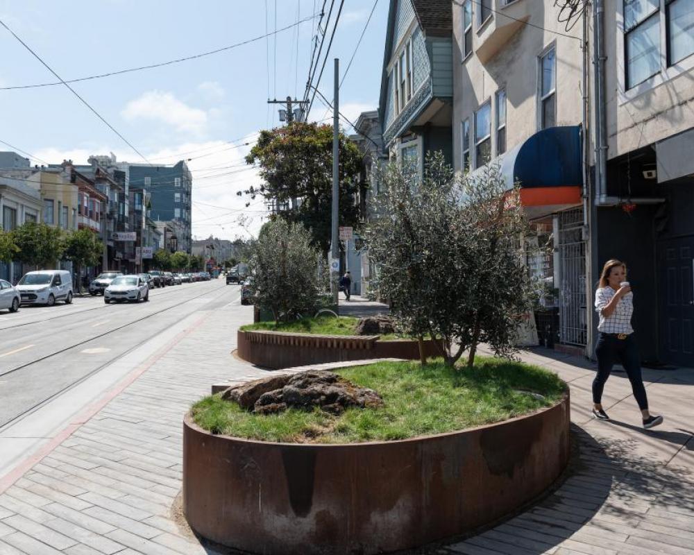 A person drinking coffee walks passed planters on a landscaped transit bulb