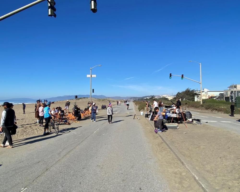 A road running alongside a beach with a crowd of people watching a band playing music.