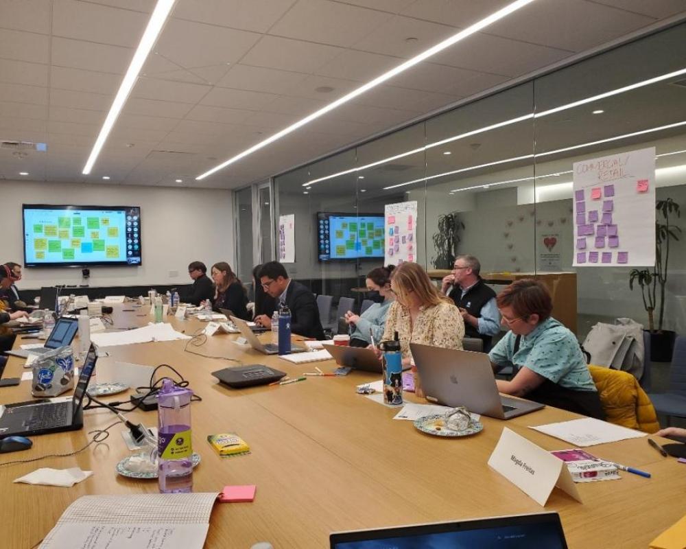 a group of people sitting at a conference table. The Working Group met the developer team in Dec 2022.