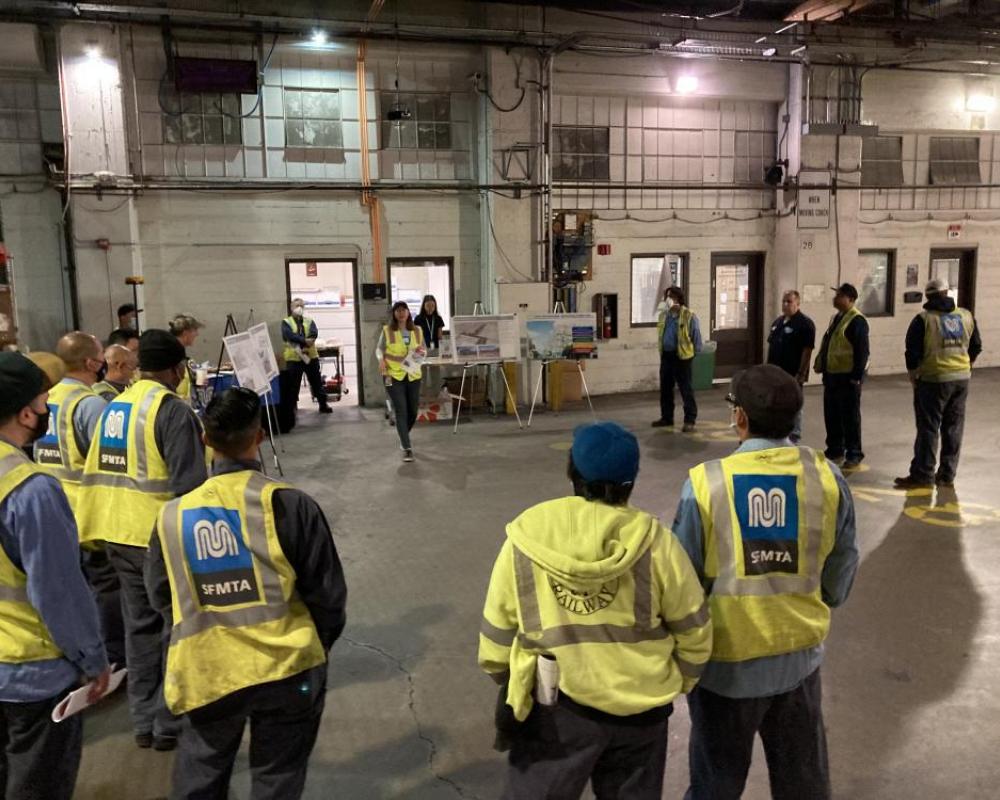 marintenance staff in yellow vests gather around a person speaking