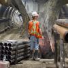 Drill casings surround a worker pausing for a bulldozer to pass during excavation of the Chinatown Station platform cavern.