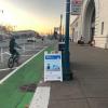 person riding bike on green bike path past Ferry Building and Quick Build sandwitch board