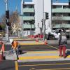A worker installs decorative pavers at a new median refuge while a woman crosses Geary and Steiner.